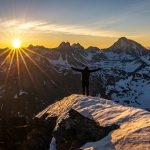 man standing on the mountain looking at the sun, indicating making it big in life