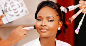 How To Apply The Perfect MakeUp A beautiful Black woman with flawless makeup sits confidently as a makeup artist applies final touches, showing how to apply the perfect makeup with precision and care.