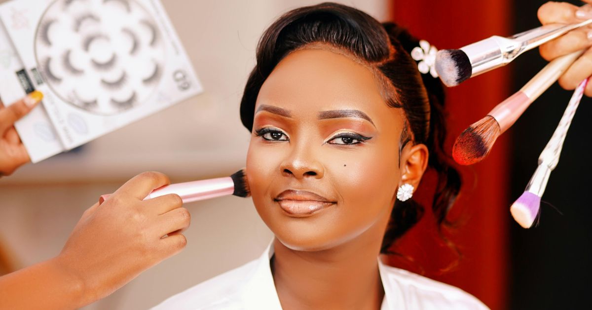A beautiful Black woman with flawless makeup sits confidently as a makeup artist applies final touches, showing how to apply the perfect makeup with precision and care.