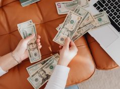 Side Hustles And Businesses To Make Money ASAP Two hands holding money beside a laptop, representing online side hustles and businesses to make money ASAP.