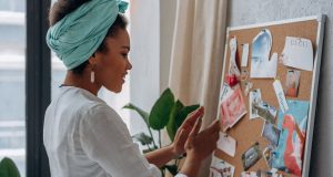 Creating Your Vision Board: Turn Your Dreams into Reality A Black woman smiling while looking at her vision board filled with photos and quotes, symbolizing creativity and purpose in creating your vision board.