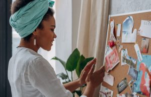 Creating Your Vision Board: Turn Your Dreams into Reality A Black woman smiling while looking at her vision board filled with photos and quotes, symbolizing creativity and purpose in creating your vision board.