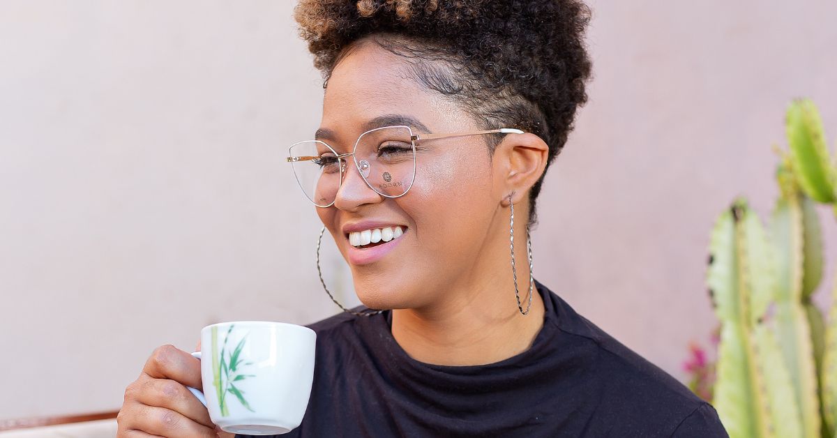 A relaxed woman smiling softly while holding a coffee cup, capturing the calm and peaceful feeling of how to live a soft life.