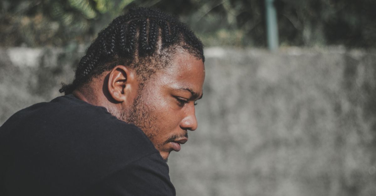 A black man with cornrows looking calm and reflective outdoors, representing how to be mentally strong and maintain resilience during life’s challenges.