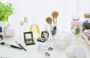 The Best Makeup Tips For Beginners Minimalist flat lay with makeup brushes, eyeshadow palette, mirror, cotton pads, notebook, and a plant on a white table — illustrating the best makeup tips for beginners.