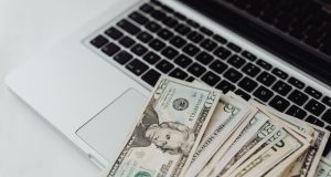 The Best Ways To Make Money Online A laptop on a table with US dollar bills spread around it, representing the best ways to make money online from home.