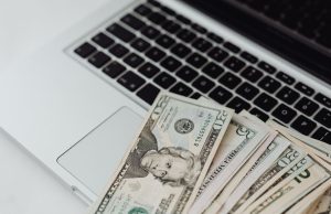 The Best Ways To Make Money Online A laptop on a table with US dollar bills spread around it, representing the best ways to make money online from home.