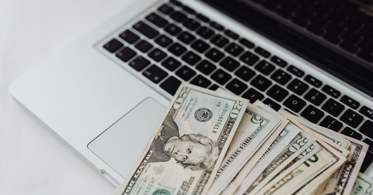 A laptop on a table with US dollar bills spread around it, representing the best ways to make money online from home.