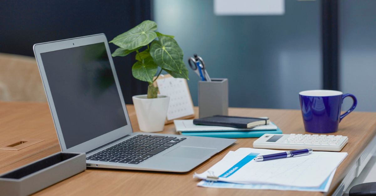 A minimal workspace with a laptop, notebook, coffee cup, calculator, and small plant — representing how to start a business with no money from home.