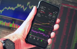 The Top 10 Stocks To Invest In For 2024 – 2025 A hand holding a smartphone displaying an AAPL stock market chart with green and red trading indicators, representing the top stocks to invest in 2024–2025.