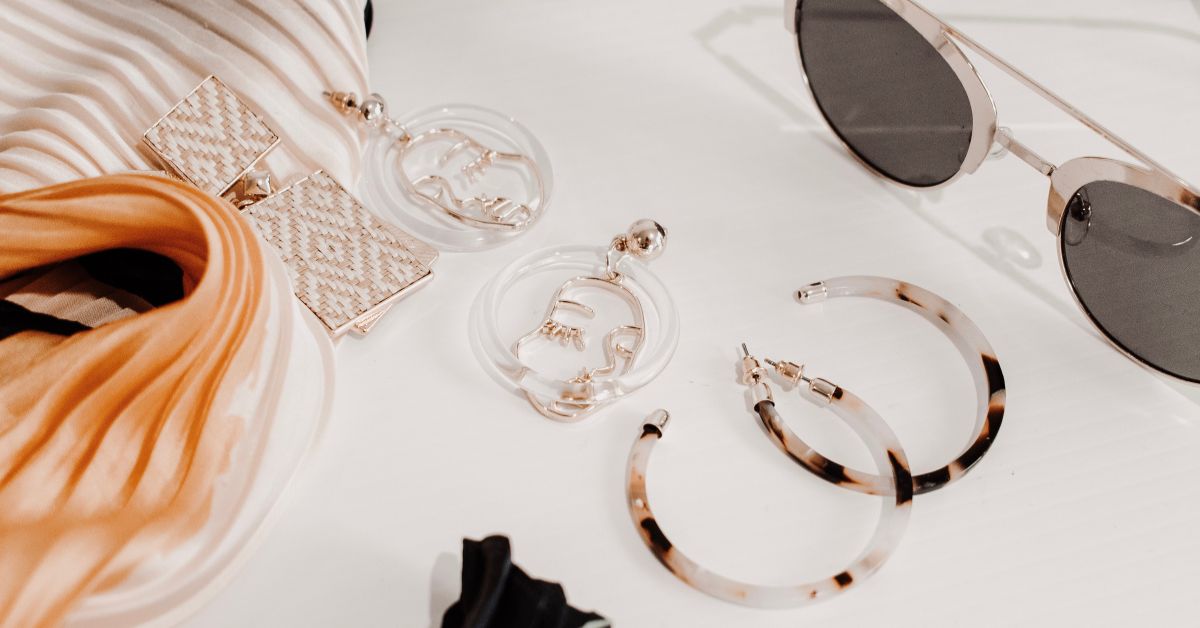 Neutral fashion accessories including jewelry and sunglasses on a white table, representing the top fashion trends for 2023 in minimalist and sustainable style.
