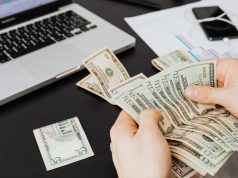 How To Get Funding For Your Business: Step-by-Step Guide for Entrepreneurs Hands counting money with laptop, document, and phone in the background, illustrating how to get funding for your business and manage finances effectively.