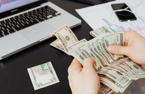 How To Get Funding For Your Business: Step-by-Step Guide for Entrepreneurs Hands counting money with laptop, document, and phone in the background, illustrating how to get funding for your business and manage finances effectively.