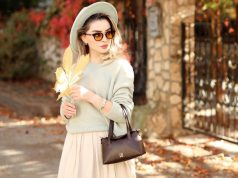 How To Look Rich And Classy On A Budget A stylish woman wearing a neutral outfit, hat, and sunglasses during autumn, holding a brown leaf with sunlight on her — showing how to look rich and classy on a budget.