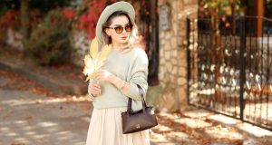 How To Look Rich And Classy On A Budget A stylish woman wearing a neutral outfit, hat, and sunglasses during autumn, holding a brown leaf with sunlight on her — showing how to look rich and classy on a budget.