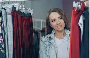 5 Effective Ways To Find Your Personal Style Woman smiling softly while browsing clothes on a rack, discovering how to find your personal style through different outfits