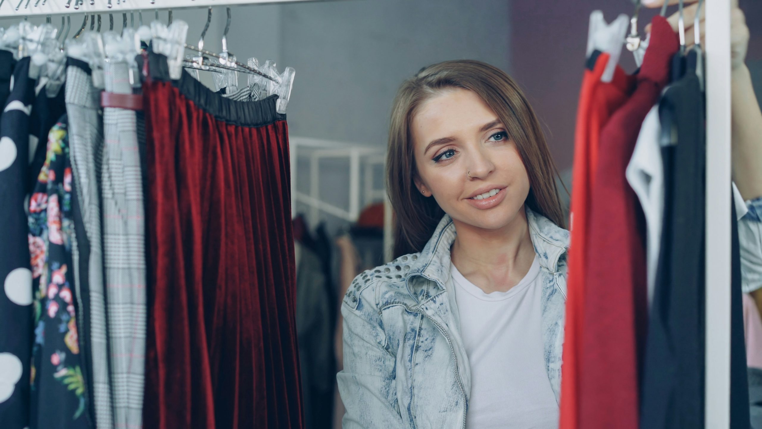 Woman smiling softly while browsing clothes on a rack, discovering how to find your personal style through different outfits
