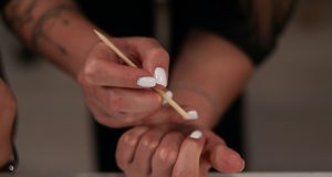 How To Do Your Own Gel Nails At Home Close-up of a woman doing her own gel nails at home, applying white gel polish with a wooden manicure stick — representing self-care, beauty, and how to do your own gel nails at home.