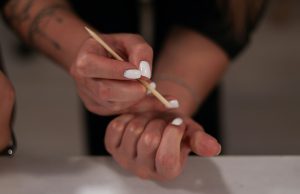 How To Do Your Own Gel Nails At Home Close-up of a woman doing her own gel nails at home, applying white gel polish with a wooden manicure stick — representing self-care, beauty, and how to do your own gel nails at home.