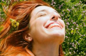 How To Stay Positive During Difficult Times A smiling woman lying on green grass under sunlight with eyes closed, symbolizing calmness and happiness — reflecting how to stay positive during difficult times.