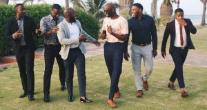 How To Style Vintage Clothes For Men Six men dressed in stylish vintage outfits, walking on a green field and laughing together, showcasing how to style vintage clothes for men with confidence and class.
