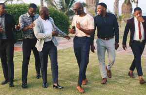 How To Style Vintage Clothes For Men Six men dressed in stylish vintage outfits, walking on a green field and laughing together, showcasing how to style vintage clothes for men with confidence and class.