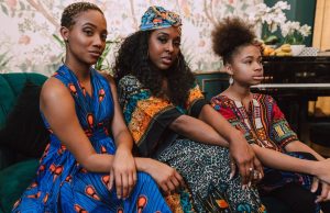 How To Style Vintage Clothes For Women Two women and a young girl in colorful Ankara prints sitting on a couch, showing how to style vintage clothes for women with African-inspired elegance.