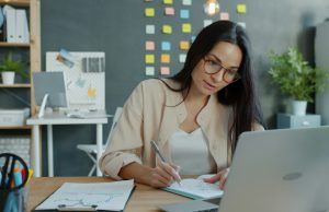 Time Management Tips For Busy Entrepreneurs A female entrepreneur working on her desk with a laptop and notebook, focused on planning her day — illustrating time management tips for busy entrepreneurs.