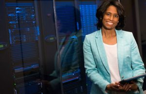 The Top 10 Cybersecurity Threats to Watch Out for in 2025 Woman in light-blue blazer holding a laptop near servers representing the top 10 cybersecurity threats to watch out for in 2025