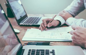 10 Mistakes to Avoid When Investing Two professionals reviewing financial plans on laptops and paper documents, discussing 10 mistakes to avoid when investing.