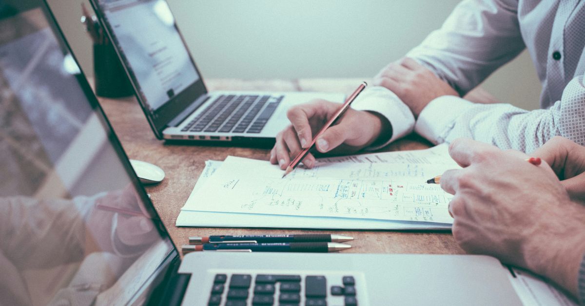 Two professionals reviewing financial plans on laptops and paper documents, discussing 10 mistakes to avoid when investing.