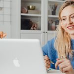 A woman using Google Gemini AI for remote work productivity, smiling while working on her laptop with a pencil in hand.