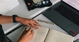 The Ultimate Guide to Writing an ATS-Friendly Resume for International Remote Jobs close-up image of woman's hands writing a resume on notebook and laptop, illustrating the Ultimate Guide to Writing an ATS-Friendly Resume for International Remote Jobs