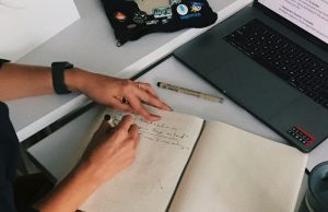 The Ultimate Guide to Writing an ATS-Friendly Resume for International Remote Jobs close-up image of woman's hands writing a resume on notebook and laptop, illustrating the Ultimate Guide to Writing an ATS-Friendly Resume for International Remote Jobs