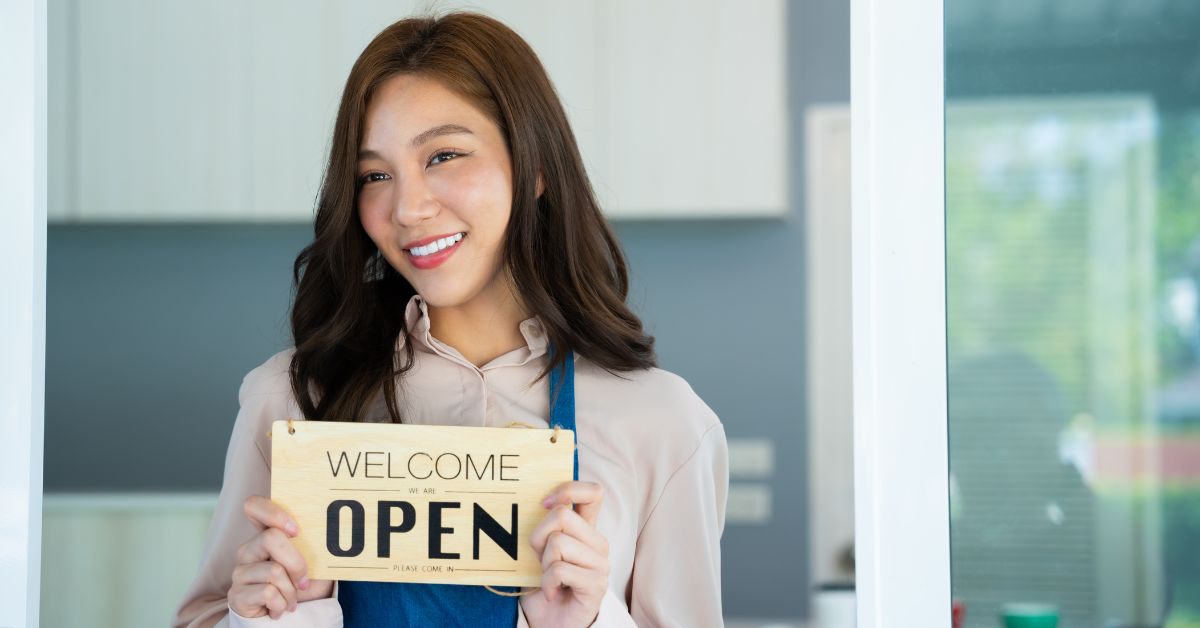 Smiling female entrepreneur standing in front of her open store, symbolizing business growth and opportunity.