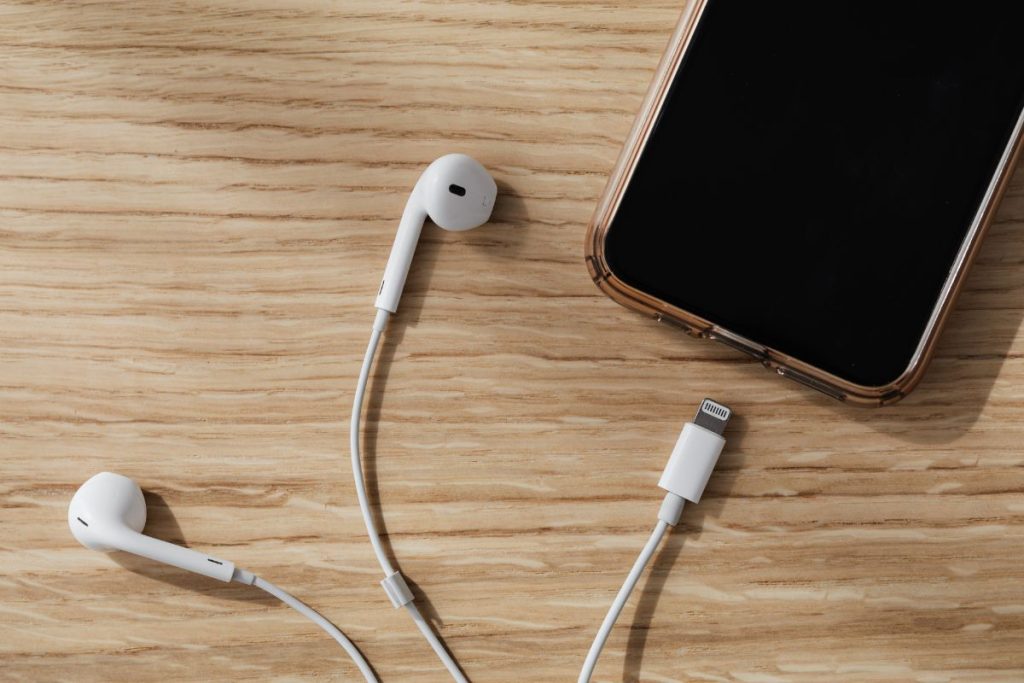 Close-up of smartphone and earpiece near charging port on wooden table, illustrating everyday habits that damage your gadgets.