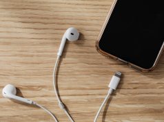 8 Everyday Habits That Damage Your Gadgets Without You Realizing It Close-up of smartphone and earpiece near charging port on wooden table, illustrating everyday habits that damage your gadgets.