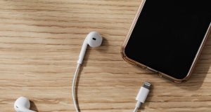 8 Everyday Habits That Damage Your Gadgets Without You Realizing It Close-up of smartphone and earpiece near charging port on wooden table, illustrating everyday habits that damage your gadgets.