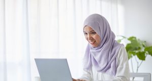 Top 10 Free AI Tools That’ll Save You Hours of Work Every Week Smiling woman working on laptop using free AI tools for productivity at home office.