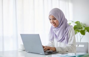 Top 10 Free AI Tools That’ll Save You Hours of Work Every Week Smiling woman working on laptop using free AI tools for productivity at home office.