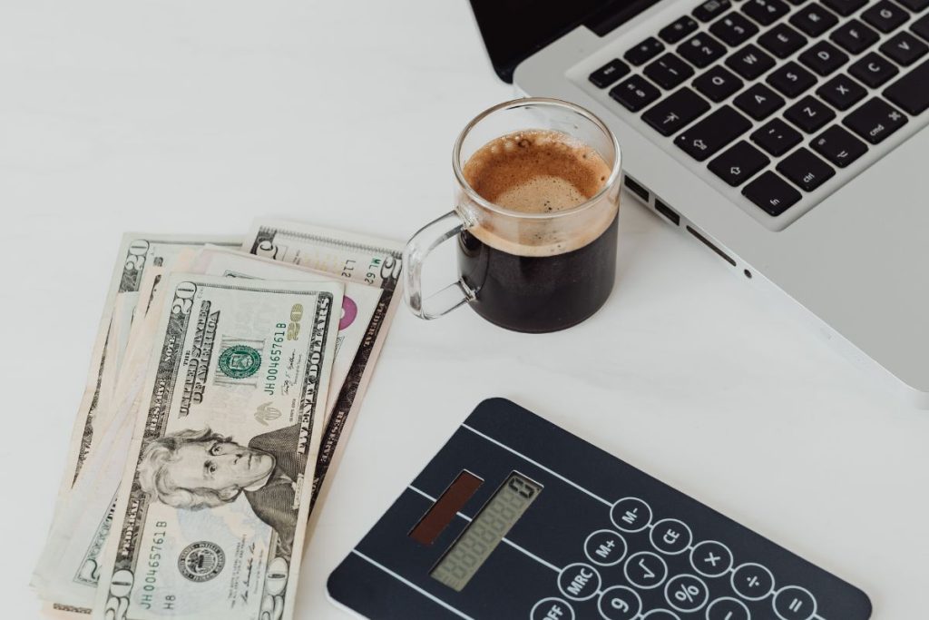 Laptop, coffee, and dollar notes on white table – how to open a dollar domiciliary account in Nigeria.