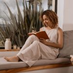 A woman enjoying a peaceful morning self-care moment, sitting by the window with a journal and pen, practicing simple self-care routines for busy women.