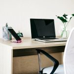 A stylish home office setup on a budget featuring a wooden desk, laptop, phone on a stand, pen holder, and vase, creating an affordable and productive workspace.