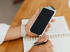 How to Check If Your Infinix or Tecno Phone Warranty Still Applies in Nigeria Hand holding a smartphone above a notebook, showing how to check Infinix or Tecno phone warranty in Nigeria