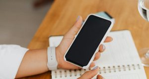 How to Check If Your Infinix or Tecno Phone Warranty Still Applies in Nigeria Hand holding a smartphone above a notebook, showing how to check Infinix or Tecno phone warranty in Nigeria