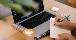 How to Set Realistic Goals and Actually Achieve Them Hands writing in a notebook beside a laptop and coffee, showing how to set realistic goals and actually achieve them