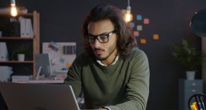 How To Start a Side Hustle While Working a 9-to-5 Man working on a laptop at home as he learns how to start a side hustle while working a 9-to-5