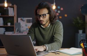 How To Start a Side Hustle While Working a 9-to-5 Man working on a laptop at home as he learns how to start a side hustle while working a 9-to-5